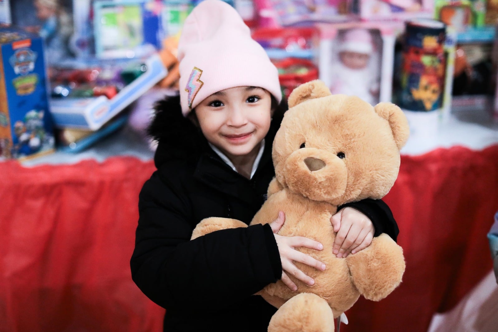 A smiling child holding a teddy bear at an Angel Tree toy shop